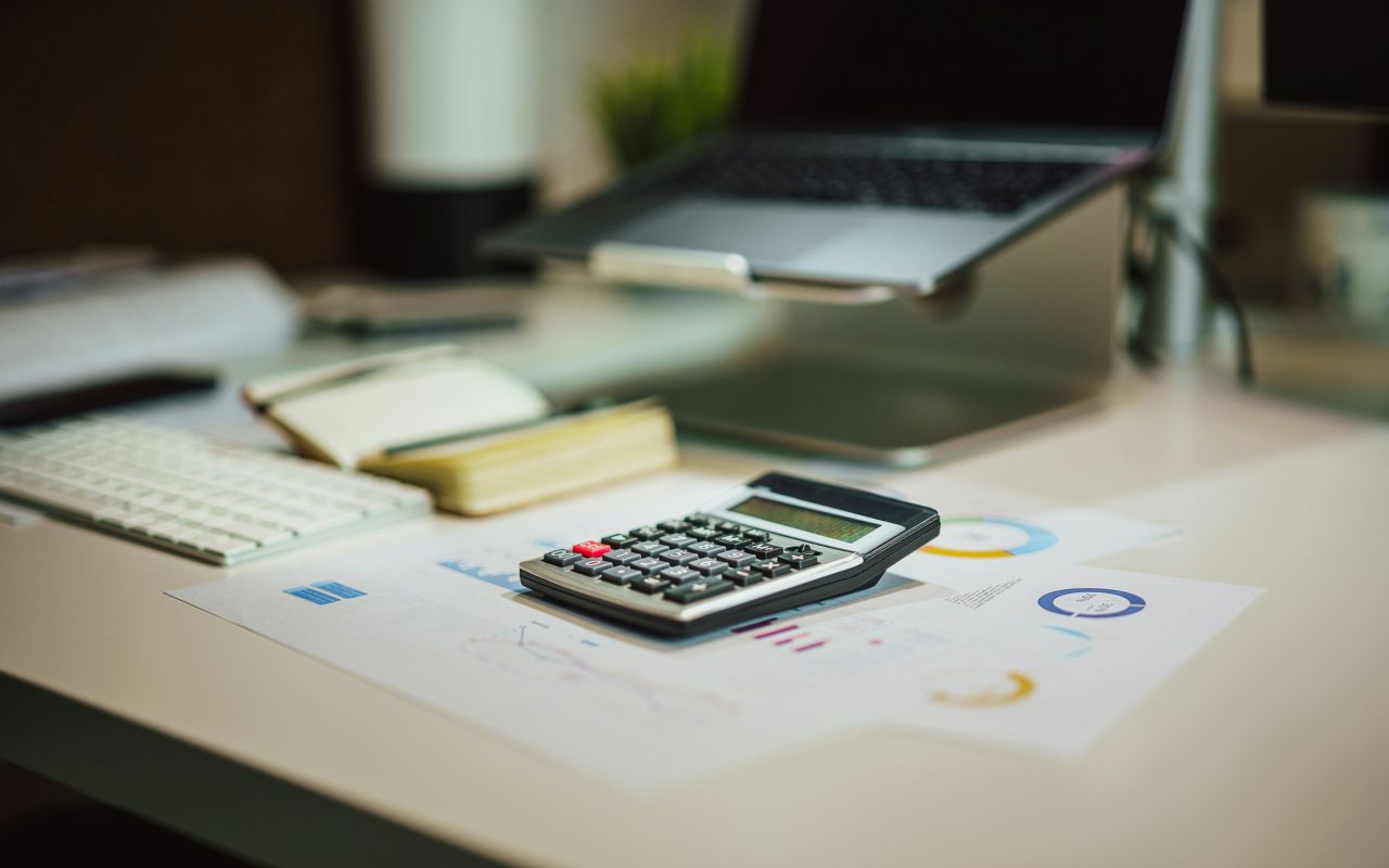 A calculator on a table next to a laptop