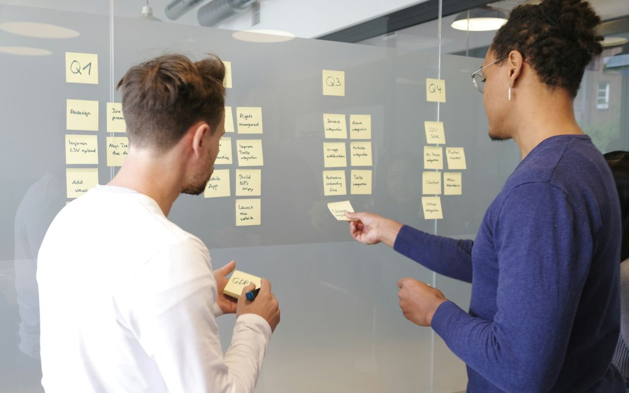 Two people planning a project with sticky notes on a glass wall